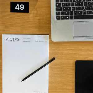 An aerial photo of white, blank note paper on a wooden table, labelled with the VICTVS logo and serial numbers at the top and bottom.