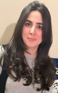 A photo of a pale skinned woman with long brown hair, smiling at the camera